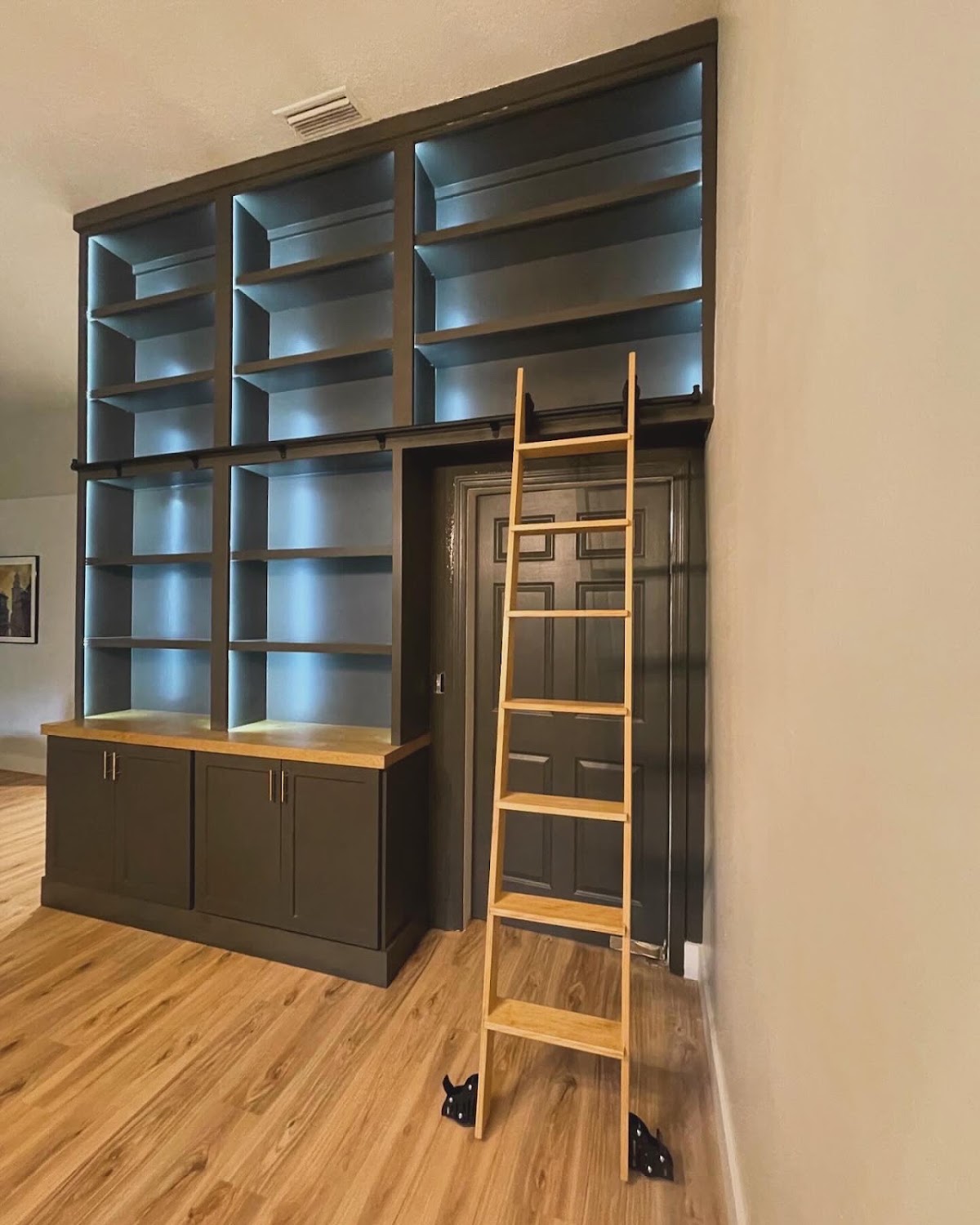 Tall dark built-in bookcase with wood library ladder and illuminated shelves