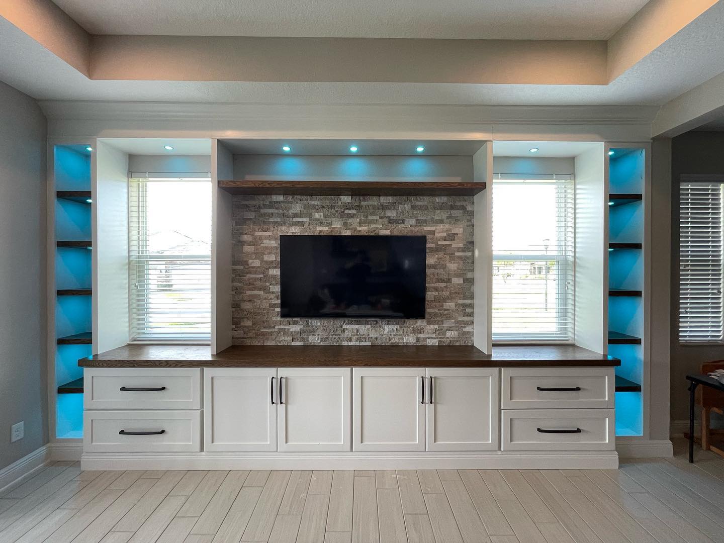 White entertainment wall with illuminated shelves, wood accents and a stone center