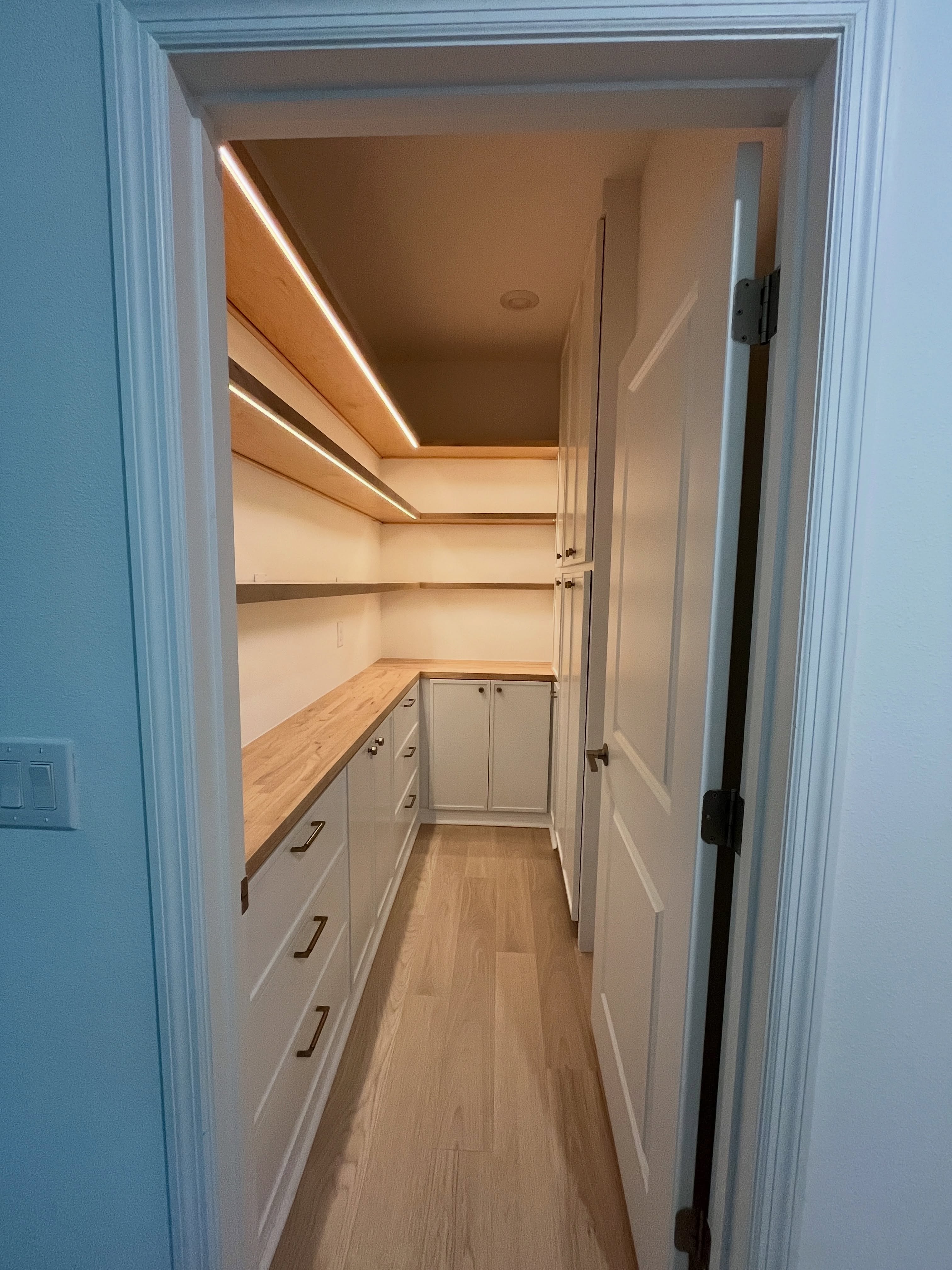 Custom pantry with white cabinets, wood counters and illuminated shelves