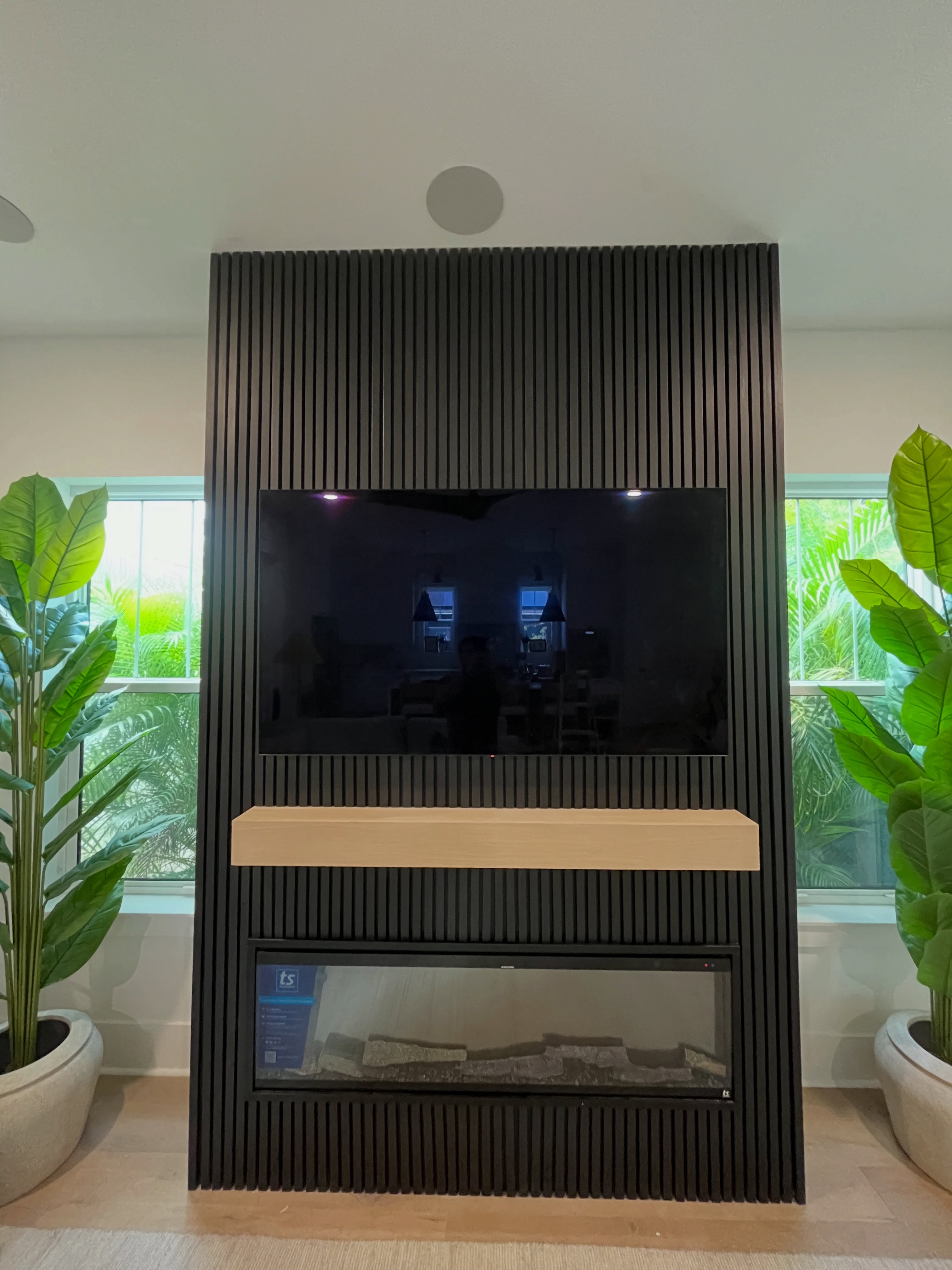 Custom dark slatted fireplace feature wall framed by windows